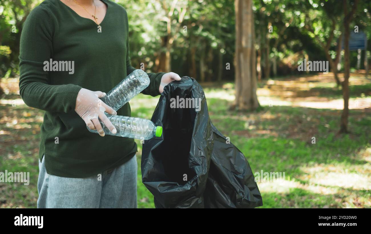 Frauen engagierter Freiwilliger nehmen an einer Umweltreinigungsaktion in einem Park Teil. Frau trägt Handschuhe und hält große schwarze Taschen. Frau Stockfoto