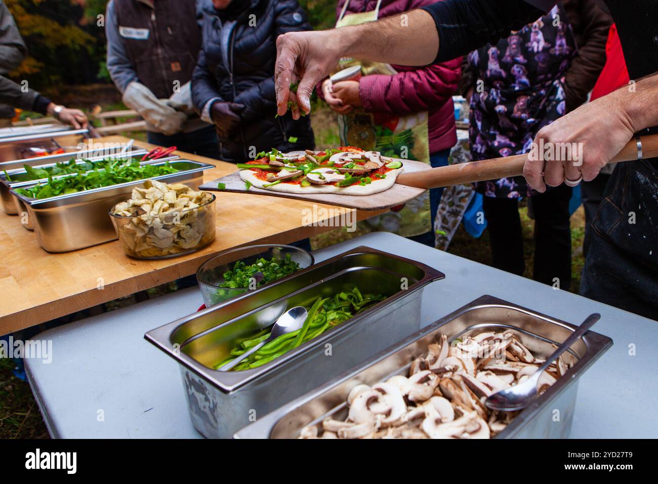 Leute fügen Dressings auf ihren frisch gekneteten Pizzateig Stockfoto