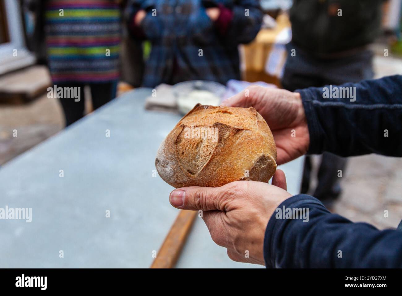 Der Mann hält einen kleinen Brotlaib, der gerade aus einem Backofen kam Stockfoto