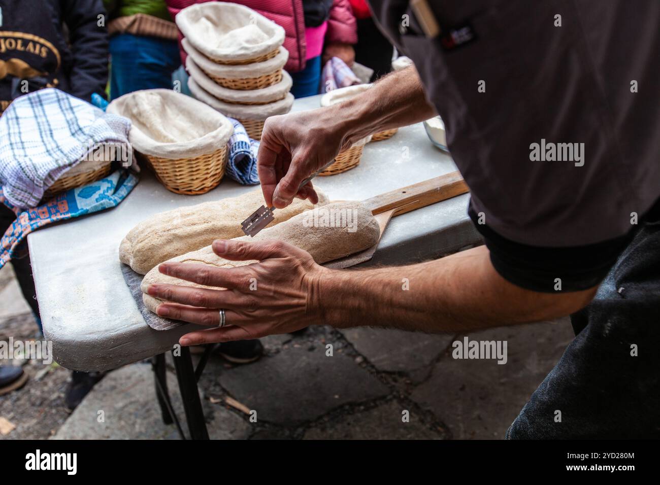 Der Mann schneidet das Brot, indem er es mit einer Rasierklinge aufschneidet, bevor er es backt Stockfoto