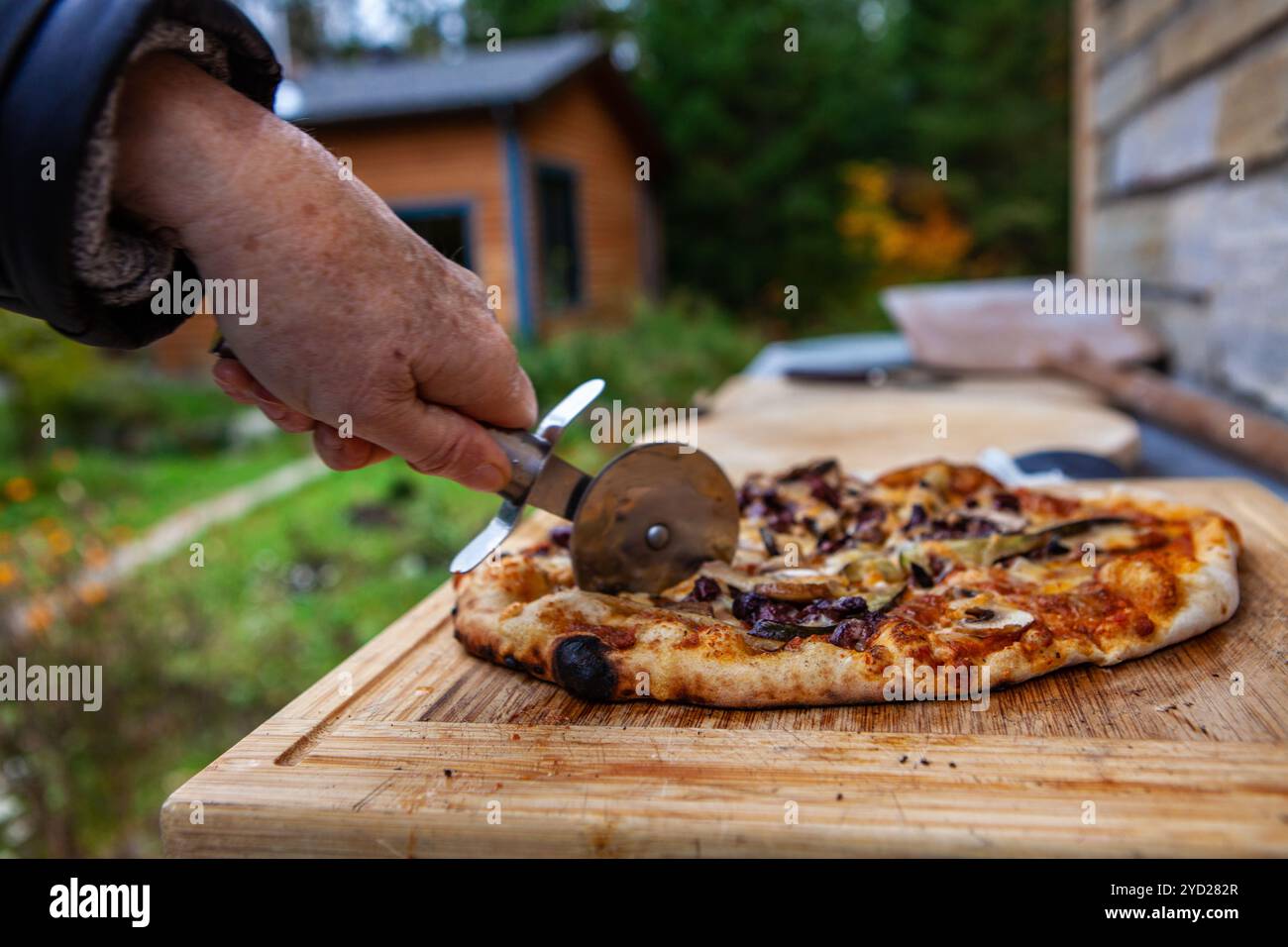 Die alte Dame schneidet eine Pizza, die gerade aus einem Brotbackofen kam Stockfoto