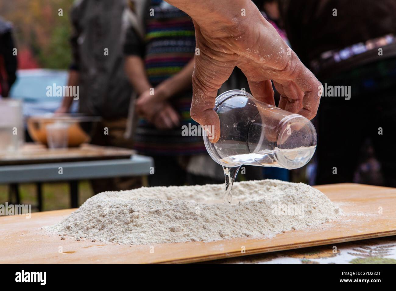 Gießen von Wasser in eine Mehlzubereitung mit der Absicht, Brot zuzubereiten Stockfoto