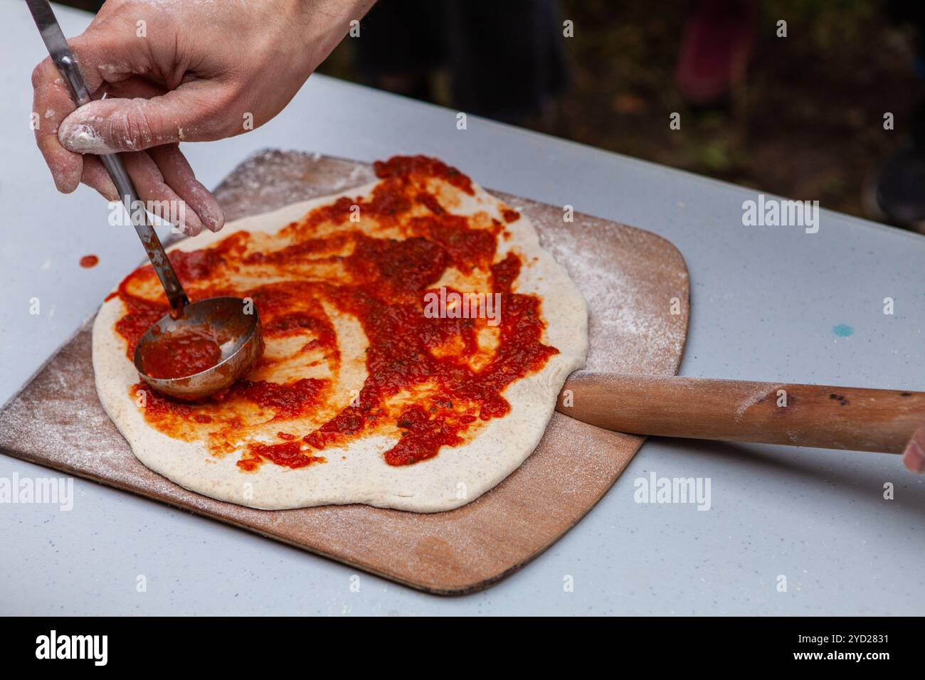 Der Mann verteilt Tomatenpaste auf frisch geknetem Pizzateig Stockfoto
