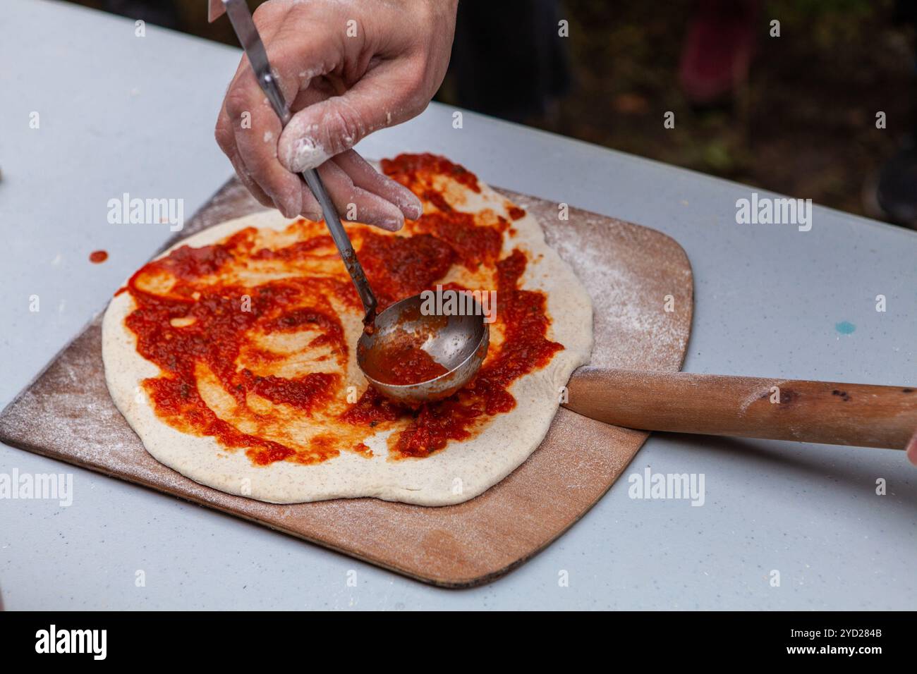 Der Mann verteilt Tomatenpaste auf frisch geknetem Pizzateig Stockfoto