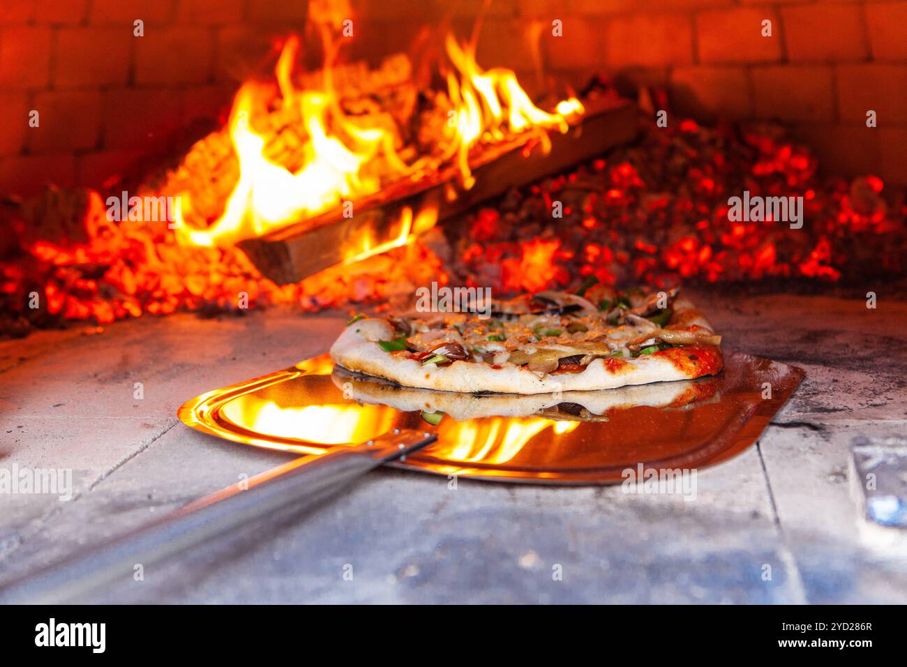 Der Mann stellt eine frisch zubereitete Pizza in einen Brotbackofen Stockfoto