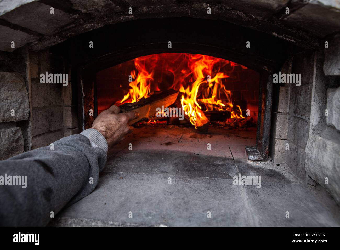 Brotbackofen mit einem Feuer im Inneren, während der Mensch Holz zum Feuer hinzufügt Stockfoto