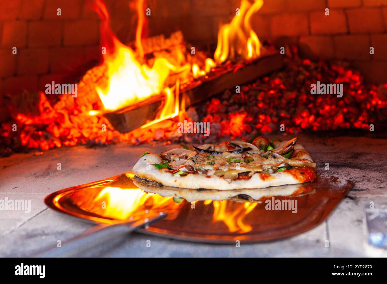 Der Mann stellt eine frisch zubereitete Pizza in einen Brotbackofen im Freien. Stockfoto