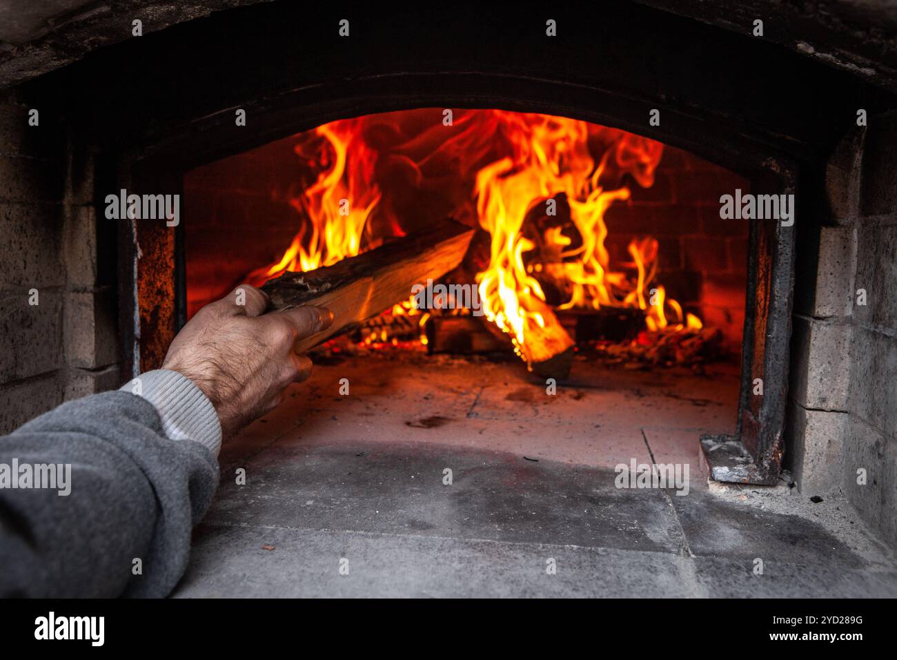 Brotbackofen mit einem Feuer im Inneren, während der Mensch Holz zum Feuer hinzufügt Stockfoto