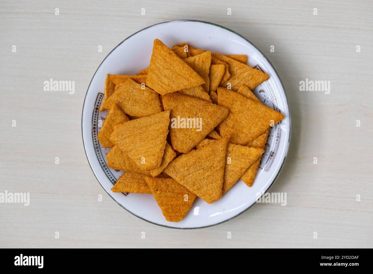 Knusprige und köstliche dreieckige Tortilla-Chips auf einer weißen Platte im mexikanischen Nachos-Geschmack, auf einer hellen Holzoberfläche platziert. Stockfoto