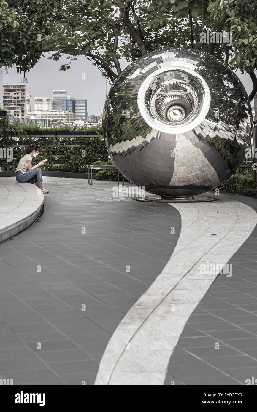 Bangkok, Thailand - 28. September 2024 - eine unbekannte junge Frau, die ein eifarbiges T-Shirt mit Jeans und Schutzmaske trägt und ein Smartphone benutzt Stockfoto