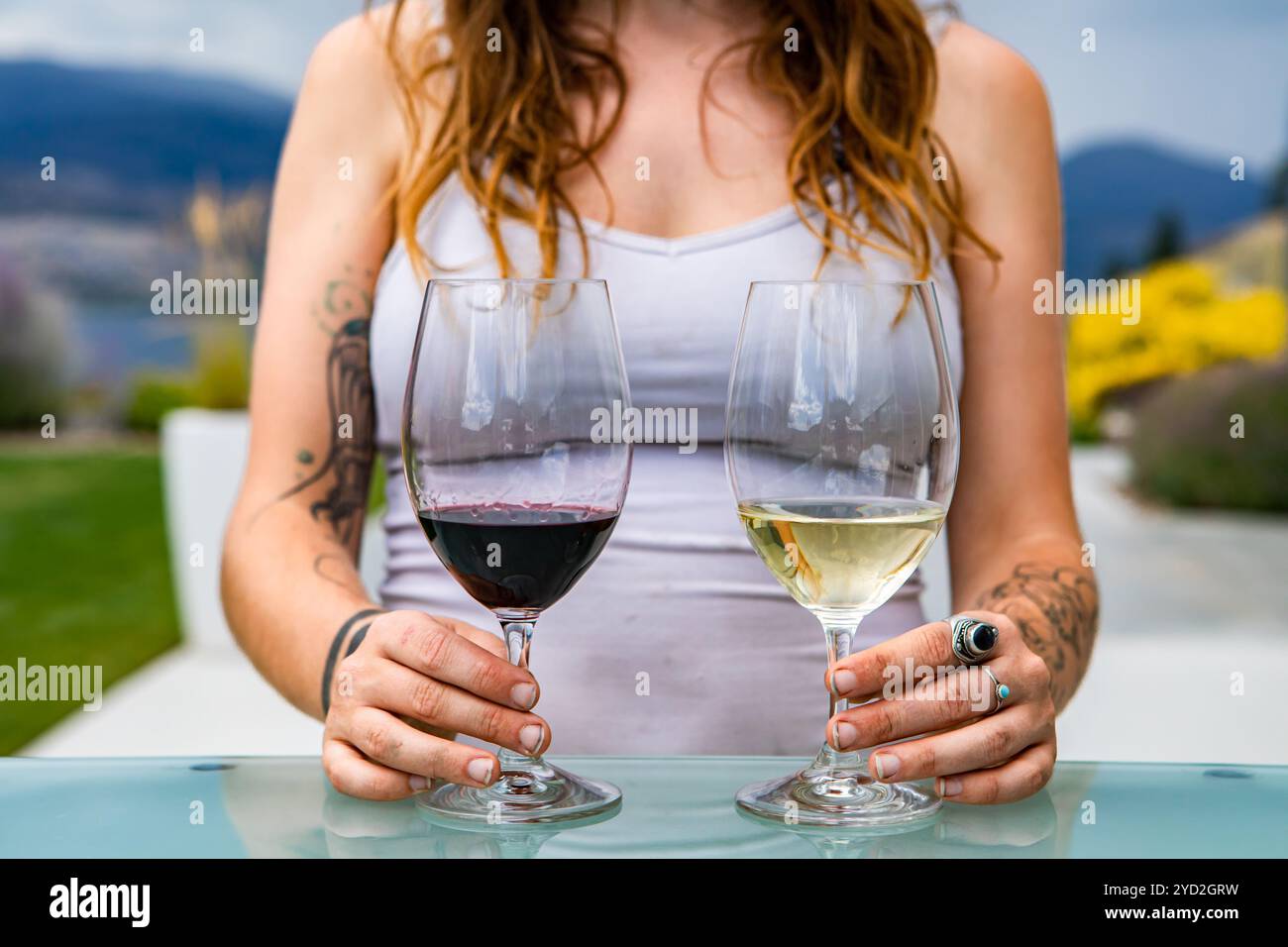 Nicht erkennbare kaukasische Frau Hände mit Tattoos auf Paar Rotwein und Weißwein Gläser, verschiedene Weine Weinprobe Auswahl Vergleich Konzept Stockfoto