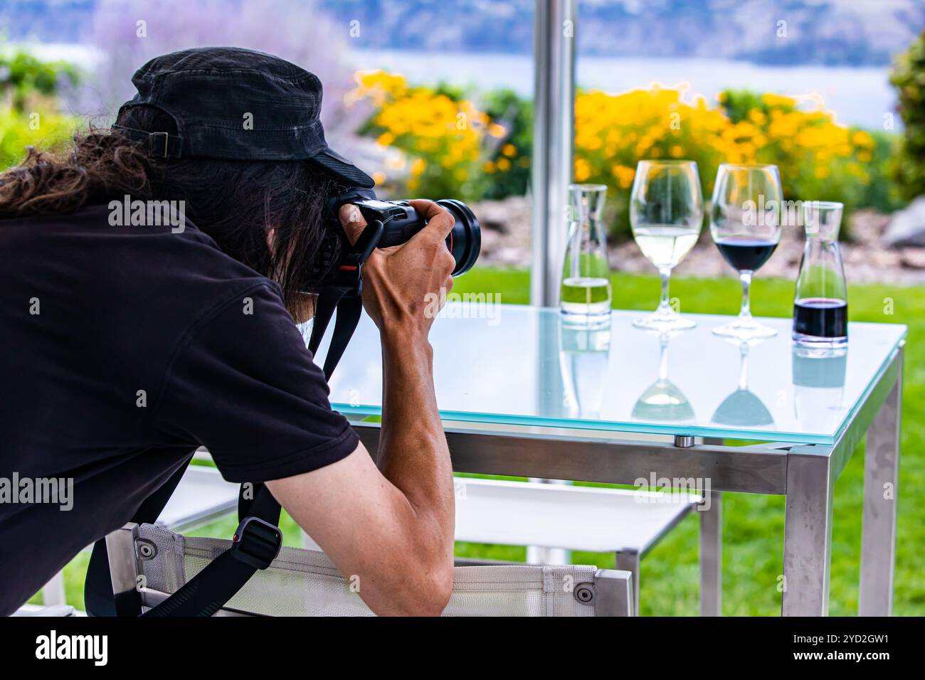 Mann Fotograf mit langem Haar mit schwarzen Rückseite Rückseite wie er Fotos von weingläser mit einem professionellen DSLR-Kamera, Wein Weingut Konzept Stockfoto