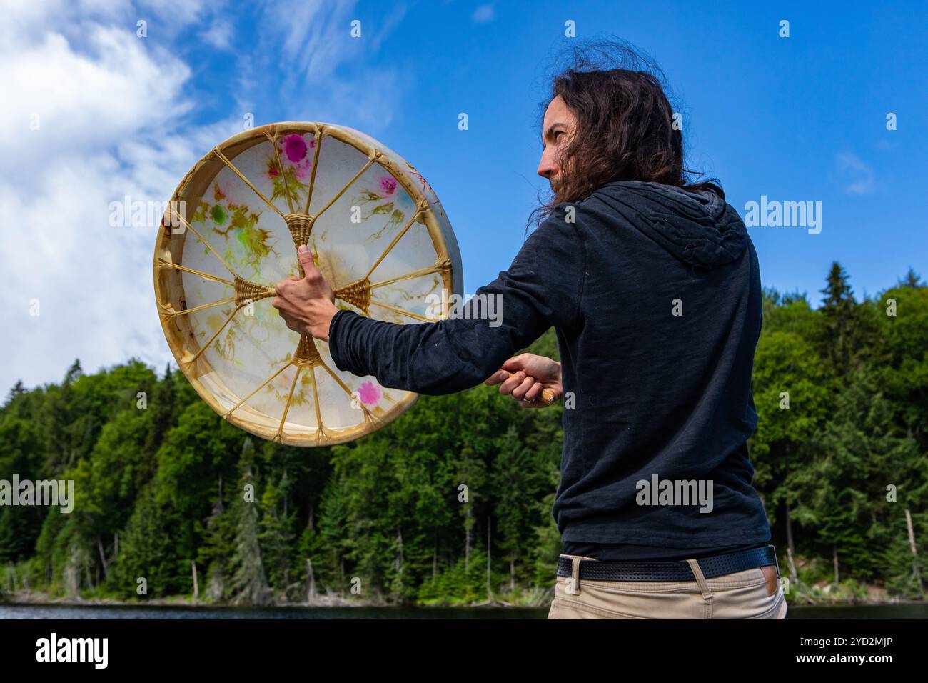 Schamanischer Mann, der heilige Trommel mit Stock spielt Stockfoto