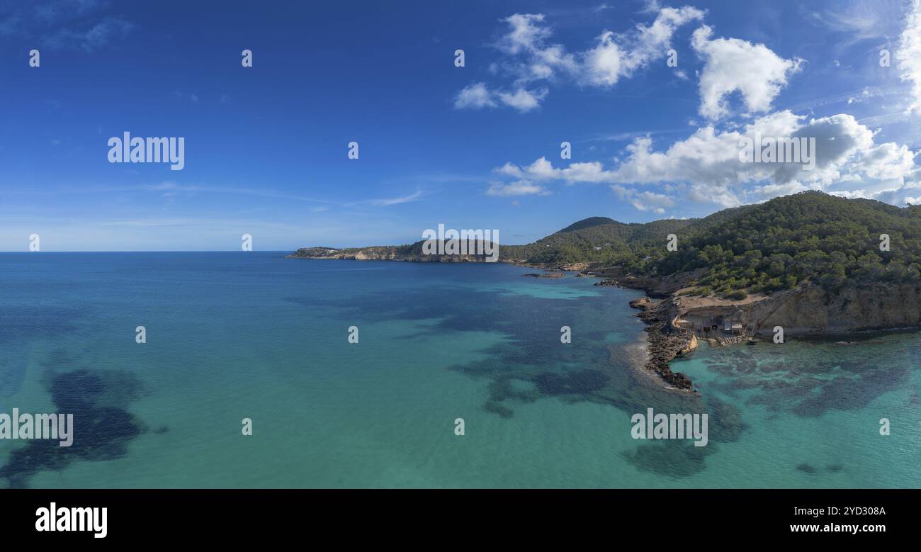 Aus der Vogelperspektive die grüne und zerklüftete hügelige Küste von Nord-Ibiza mit dem türkisfarbenen Wasser der Bucht Cala Xarraca Stockfoto