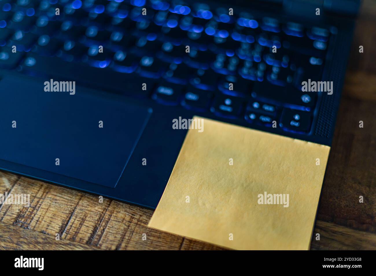 Eine gelbe Haftnotiz befindet sich auf der Unterseite einer Laptop-Tastatur. Die Notiz kann eine Erinnerung, eine Aufgabenliste oder eine Nachricht an den Benutzer sein Stockfoto