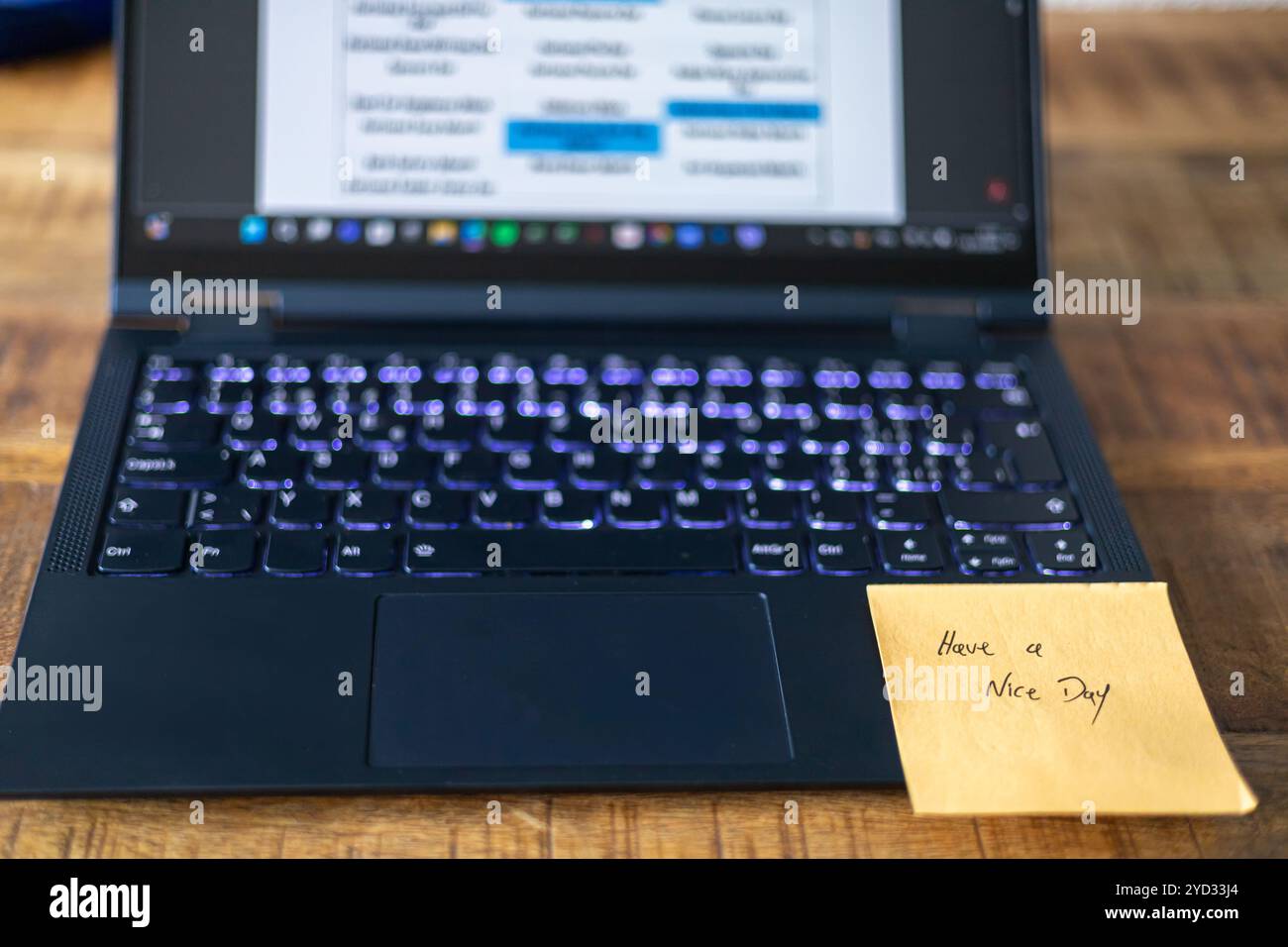 Ein Notebook mit einem Haftnotiz, auf dem steht: „Ich wünsche dir einen schönen Tag“. Der Laptop ist geöffnet und der Bildschirm leuchtet Stockfoto