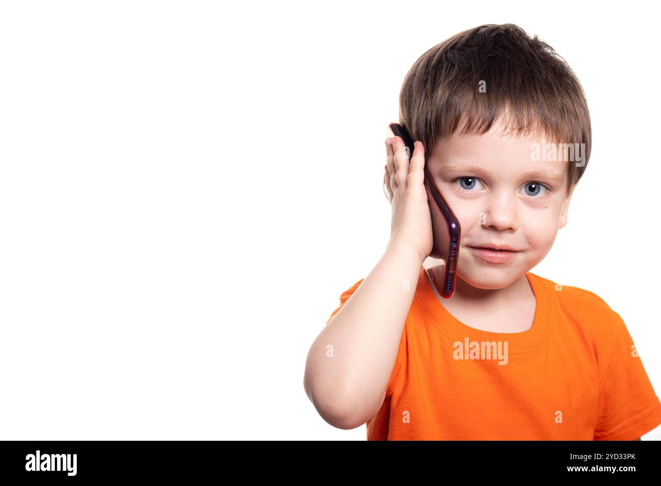 Ein kleiner Junge mit einem Telefon auf weißem Hintergrund. Telefon für Jungen. Die Kinder von heute. Verbindung mit dem Kind. Vorteile und Schaden Stockfoto