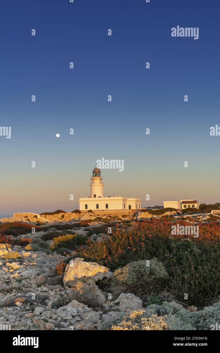 Ein vertikaler Blick auf den Leuchtturm von Cap de Cavalleria auf Menorca bei Sonnenuntergang bei aufsteigendem Vollmond Stockfoto