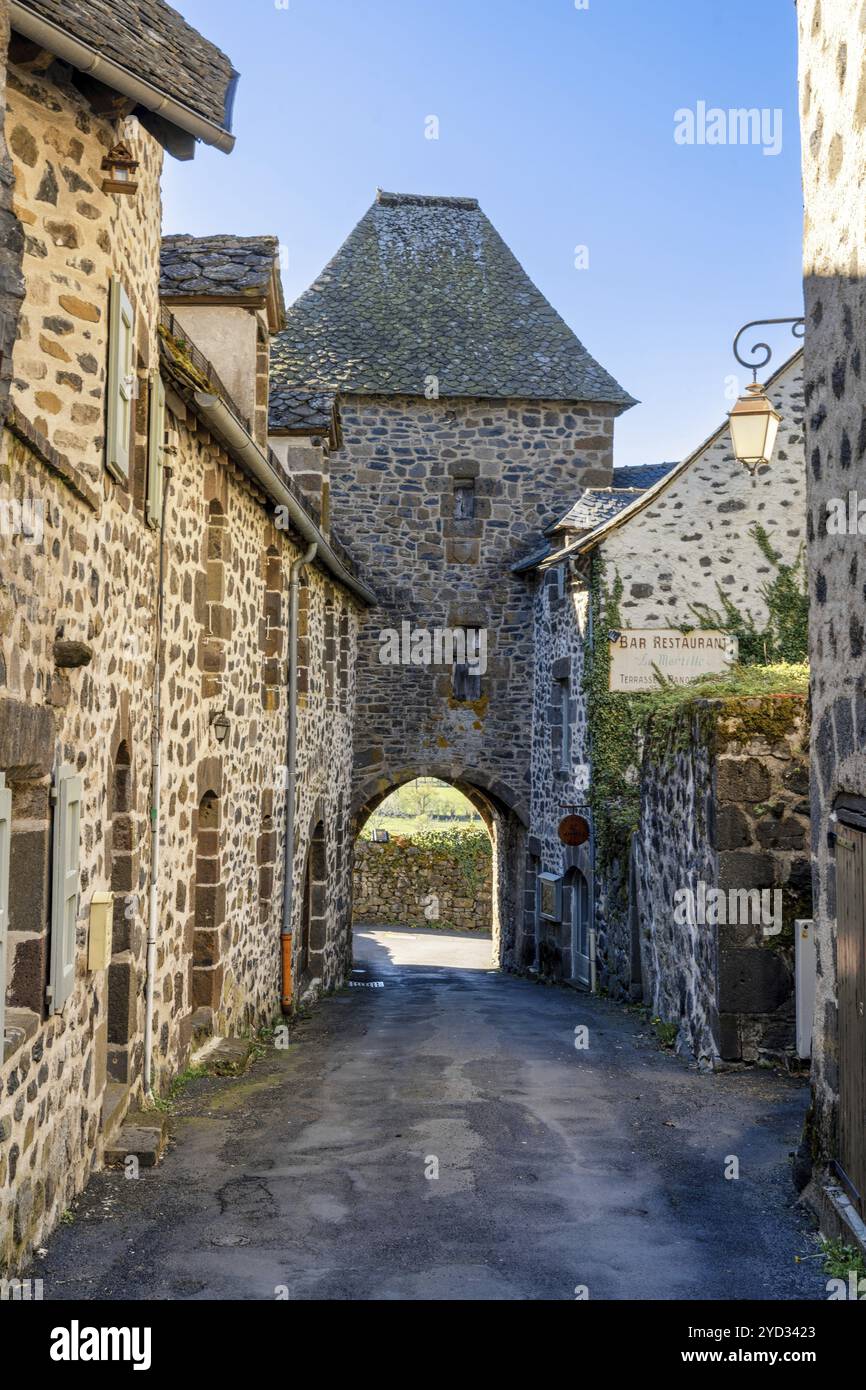 Salers, Frankreich, 19. März 2024: Enge Straße mit Stadttor und Wachturm in der malerischen Ortschaft Salers in Mittelfrankreich, Europa Stockfoto