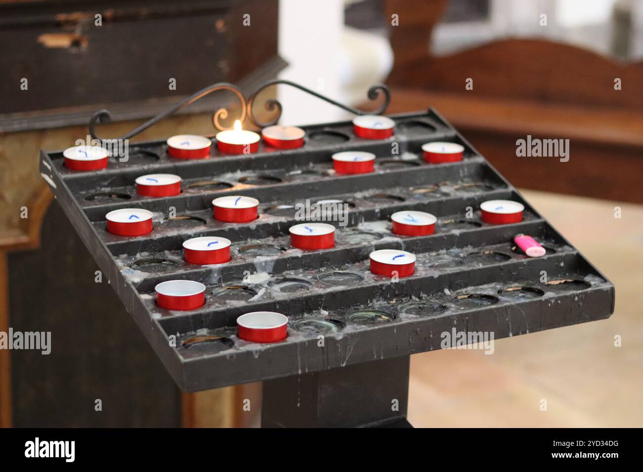 Votivstand in einer Kirche, gefüllt mit kleinen roten Kerzen Stockfoto