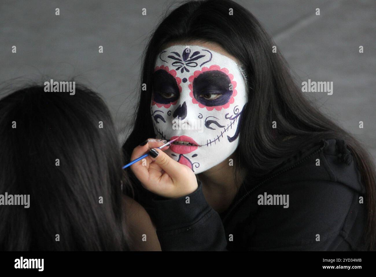 Die junge Mexikanerin schminkt catrina vor dem Spiegel, um den Tag der Toten in Mexiko zu feiern Stockfoto