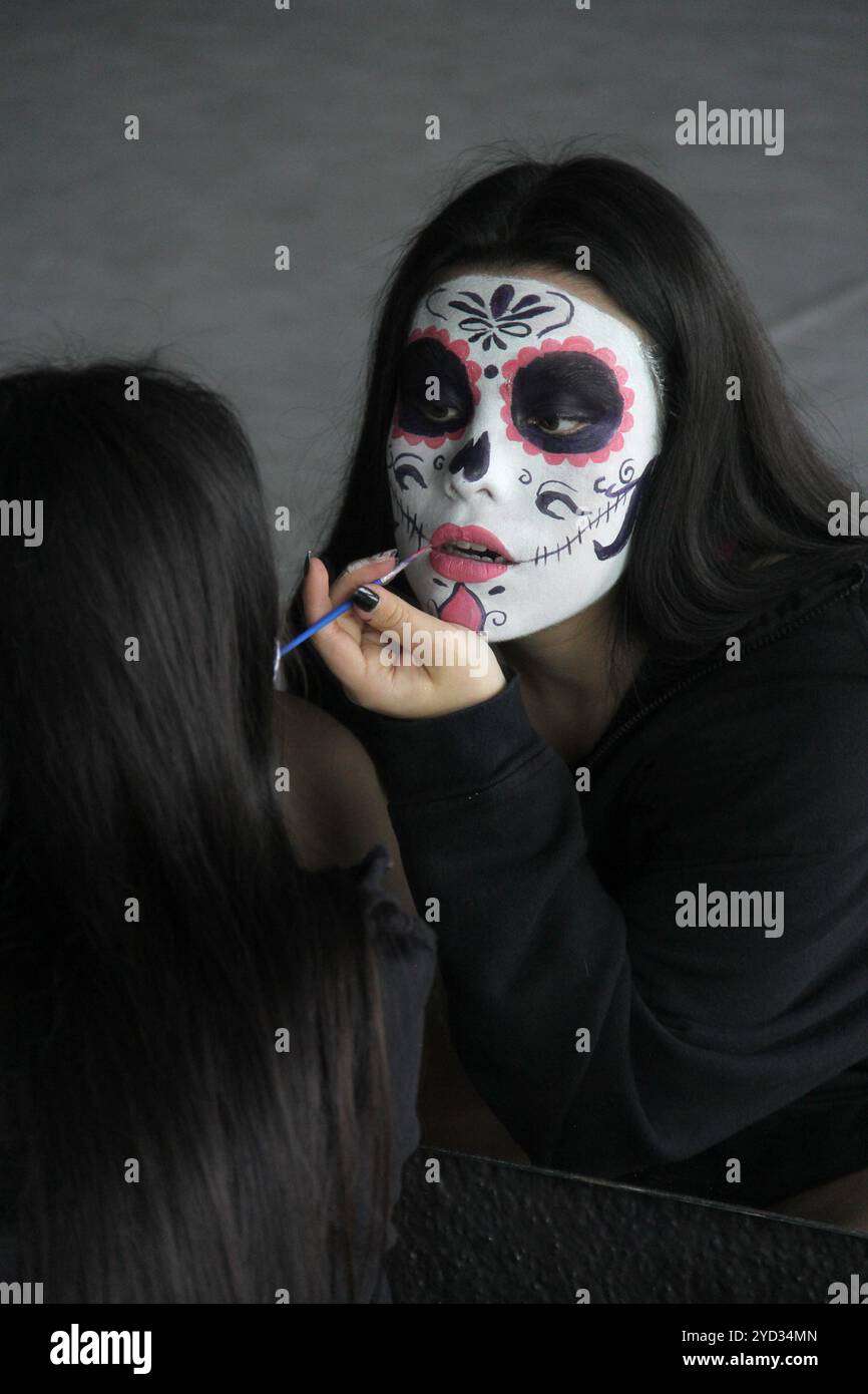 Die junge Mexikanerin schminkt catrina vor dem Spiegel, um den Tag der Toten in Mexiko zu feiern Stockfoto