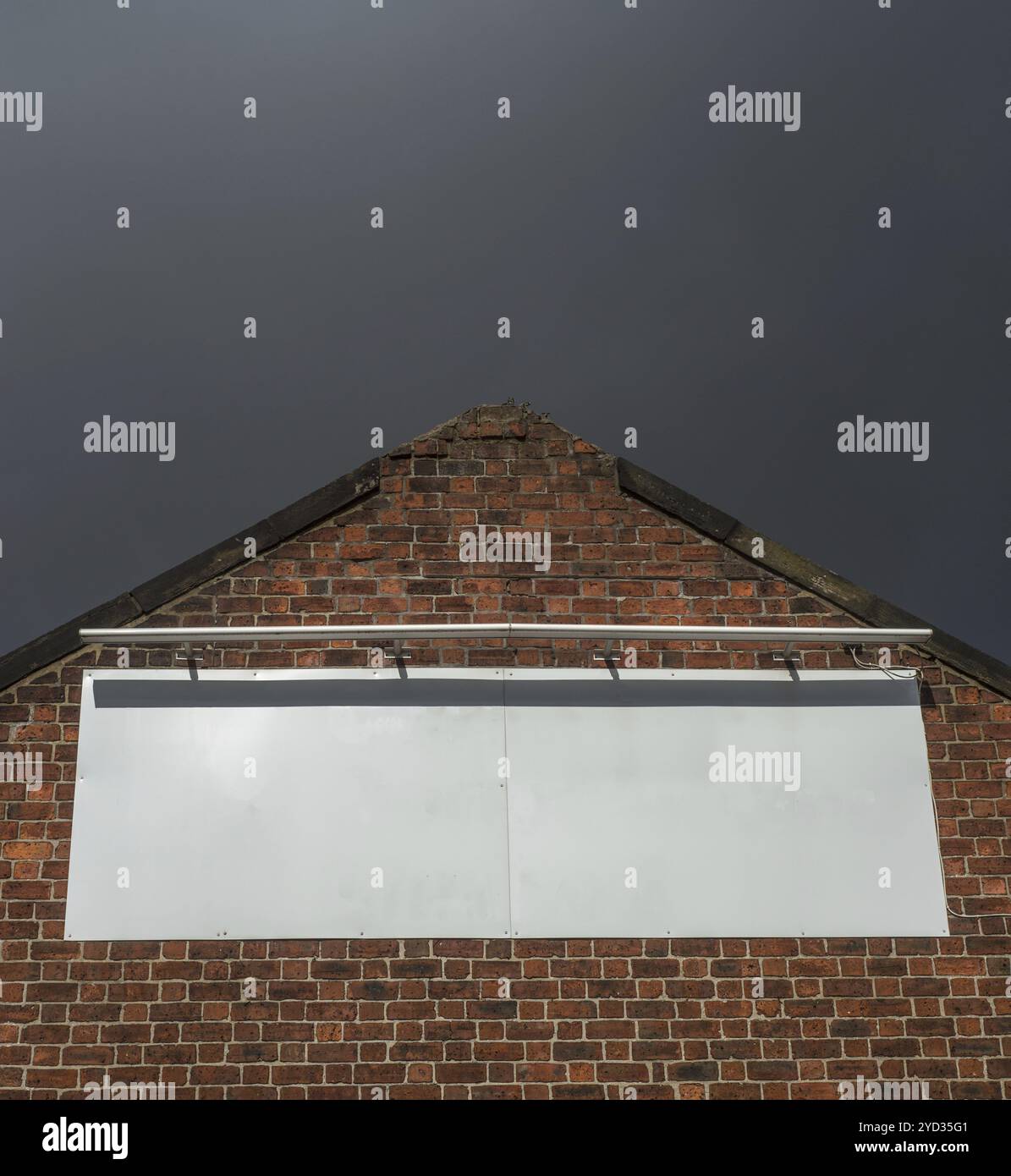 Leeres Plakatschild auf einem alten Gebäude aus roten Ziegeln mit Moody Sky Stockfoto