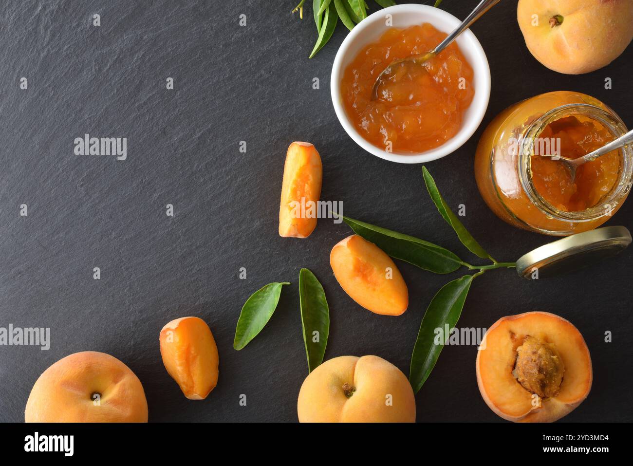 Pfirsichmarmelade, Fruchtstücke und Scheiben mit Blättern auf Schiefertisch. Draufsicht. Stockfoto
