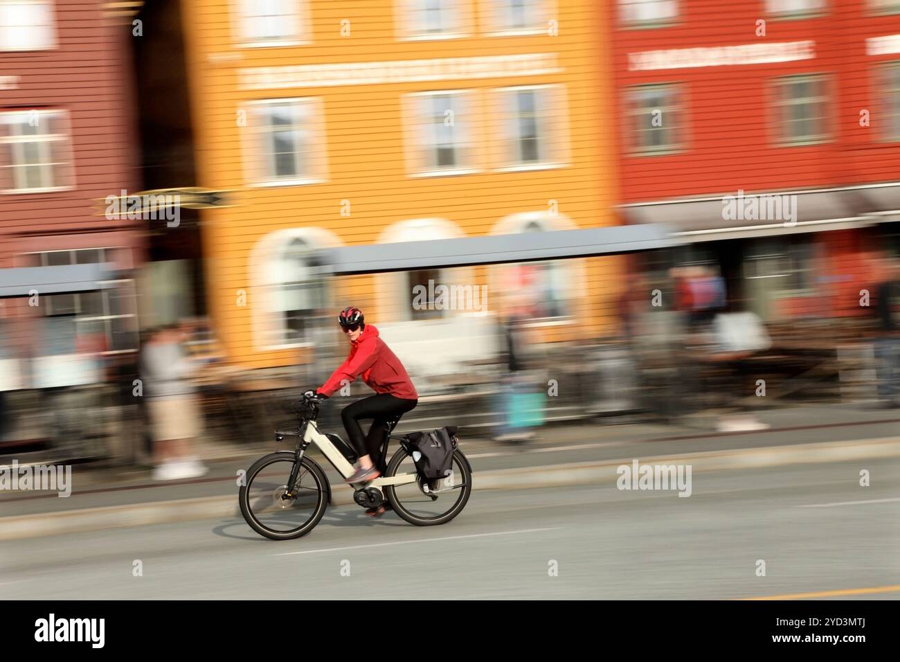 Radfahrer fahren mit dem E-Bike vorbei an traditionellen Holzhäusern an der Hanseatic Wharf, Bryggen, Bergen, Norwegen. Stockfoto