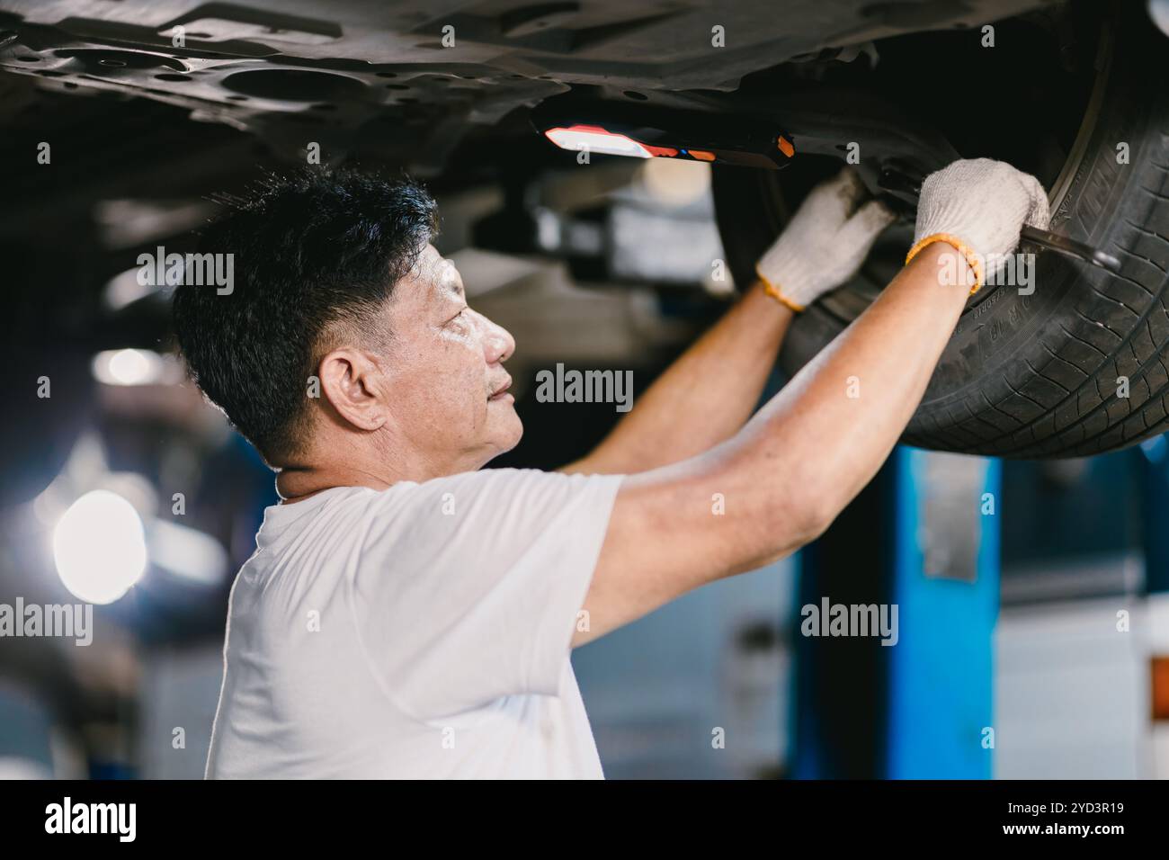 Glücklicher asiatischer Mechaniker, der Reparaturfahrzeug im Car Service arbeitet. Arbeiter, der das Aufhängungssystem unter dem Fahrzeug repariert. Stockfoto