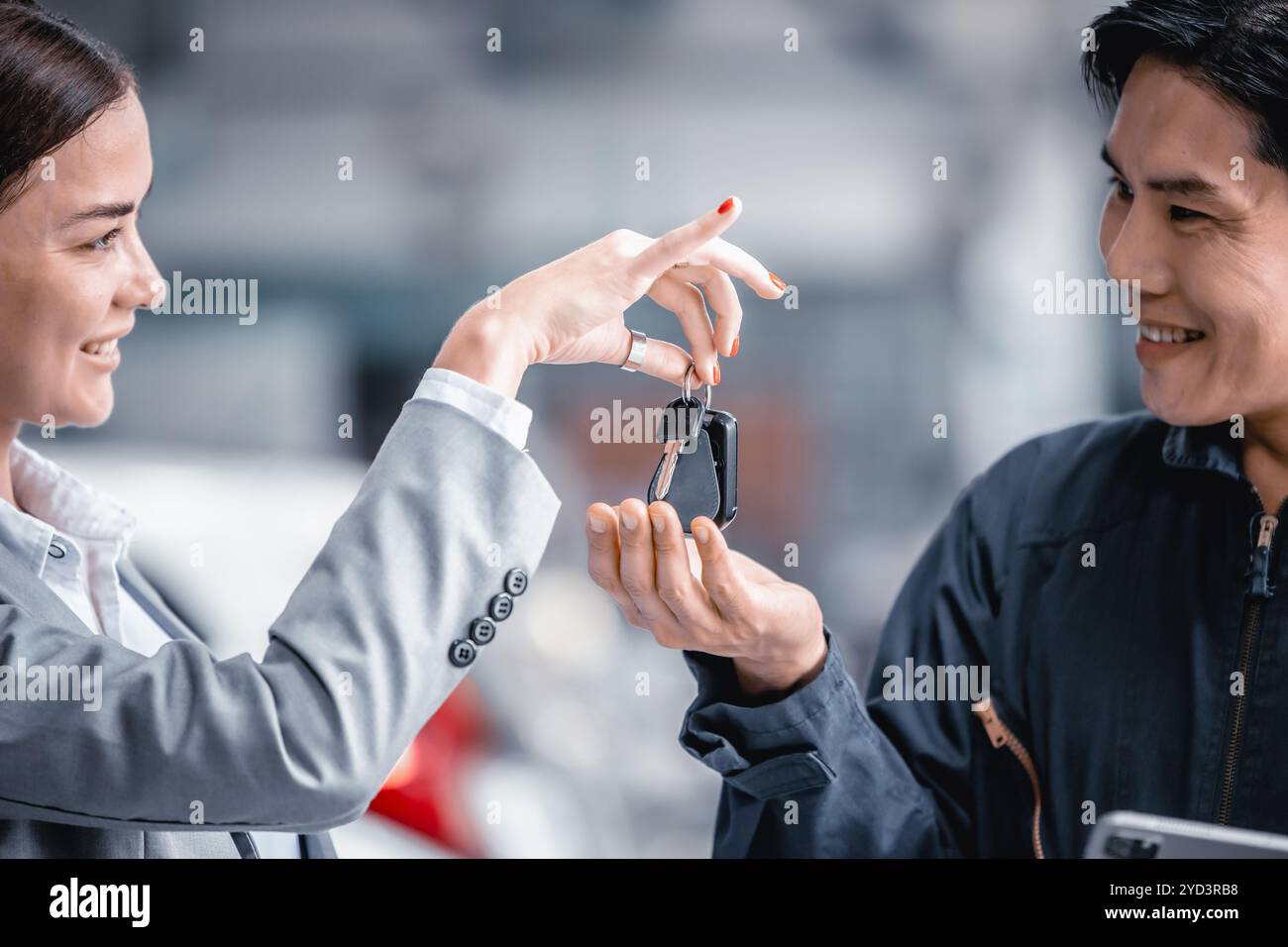 Geschäftsfrauen geben einen Autoschlüssel für das Fahrzeug, um Mechaniker zu bedienen, glücklich lächelnd in der Garage. Stockfoto