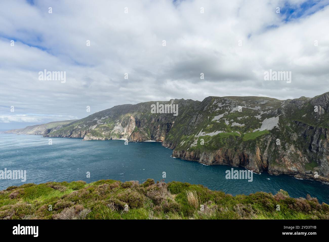 Die farbenfrohen Klippen von Slieve League, Irland, erheben sich über dem blauen Atlantik unter einem bewölkten Himmel und schaffen eine lebendige Küstenlandschaft Stockfoto