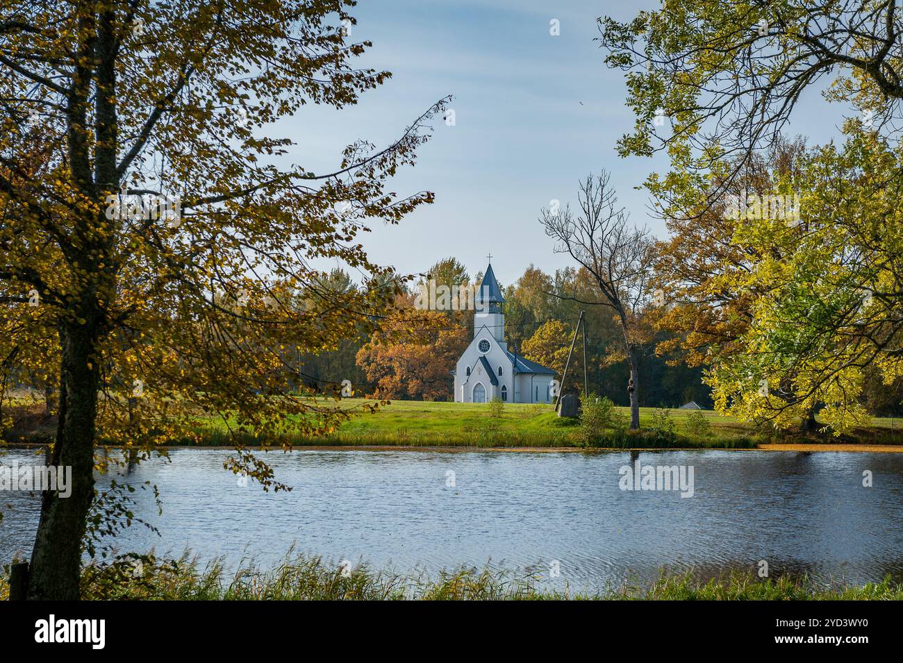 Atemberaubende Herbstlandschaft mit einer Kirche am Fluss, Herbstfarben und einem friedlichen Spaziergang am Ufer an einem warmen Tag. Stockfoto