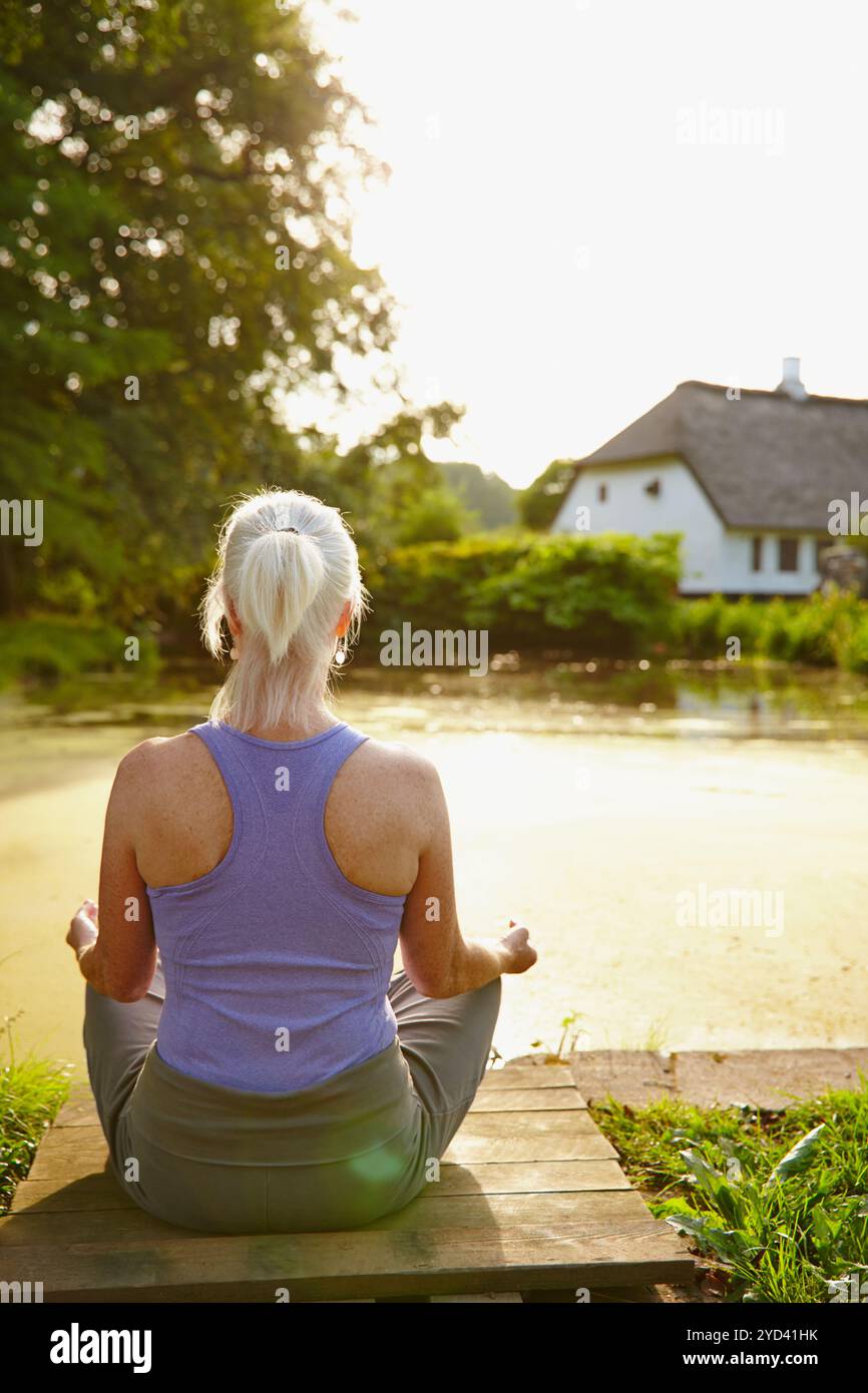 Ältere Frau, im Freien und zurück für Yoga, Meditation und Achtsamkeit für die Heilung von Chakra. Weibliche Person, Blick auf den Fluss und ganzheitliche Pose für spirituelles Stockfoto