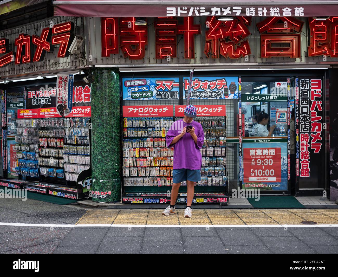 Ein Junge auf seinem Handy draußen und ein Elektronikgeschäft in Tokio, Japan. Stockfoto