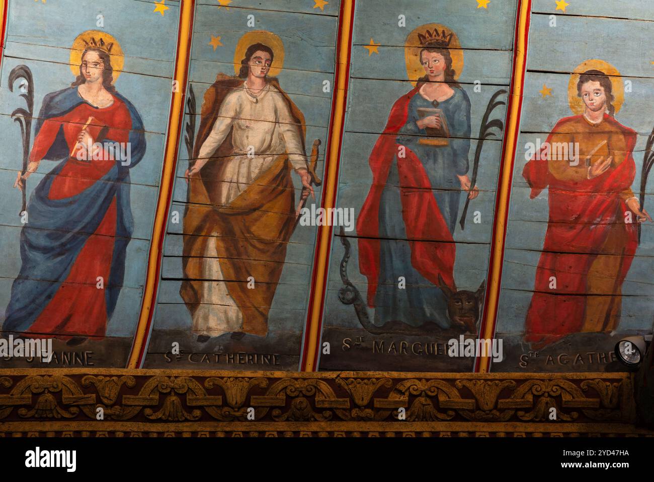 Vier weibliche Heilige, von denen jede einen Märtyrerpalmwed hält: Jeanne d’Arc (Ste Jeanne oder Jeanne d’Arc); die Heilige Katharina von Alexandria, die ein Schwert hält, Symbol ihrer Enthauptung; die Heilige Margarete von Antiochia (Ste Marguerite) mit einem Drachen zu ihren Füßen; und die Heilige Agatha von Sizilien (Ste Agathe). Sowohl Johanna von Arc als auch Margarete von Antiochia tragen Märtyrerkronen. Mitte der 1800er Jahre Gemälde auf holzgetäfeltem Deckengewölbe der Kirche Saint Nonne, Dirinon, Finistère, Bretagne, Frankreich. Stockfoto