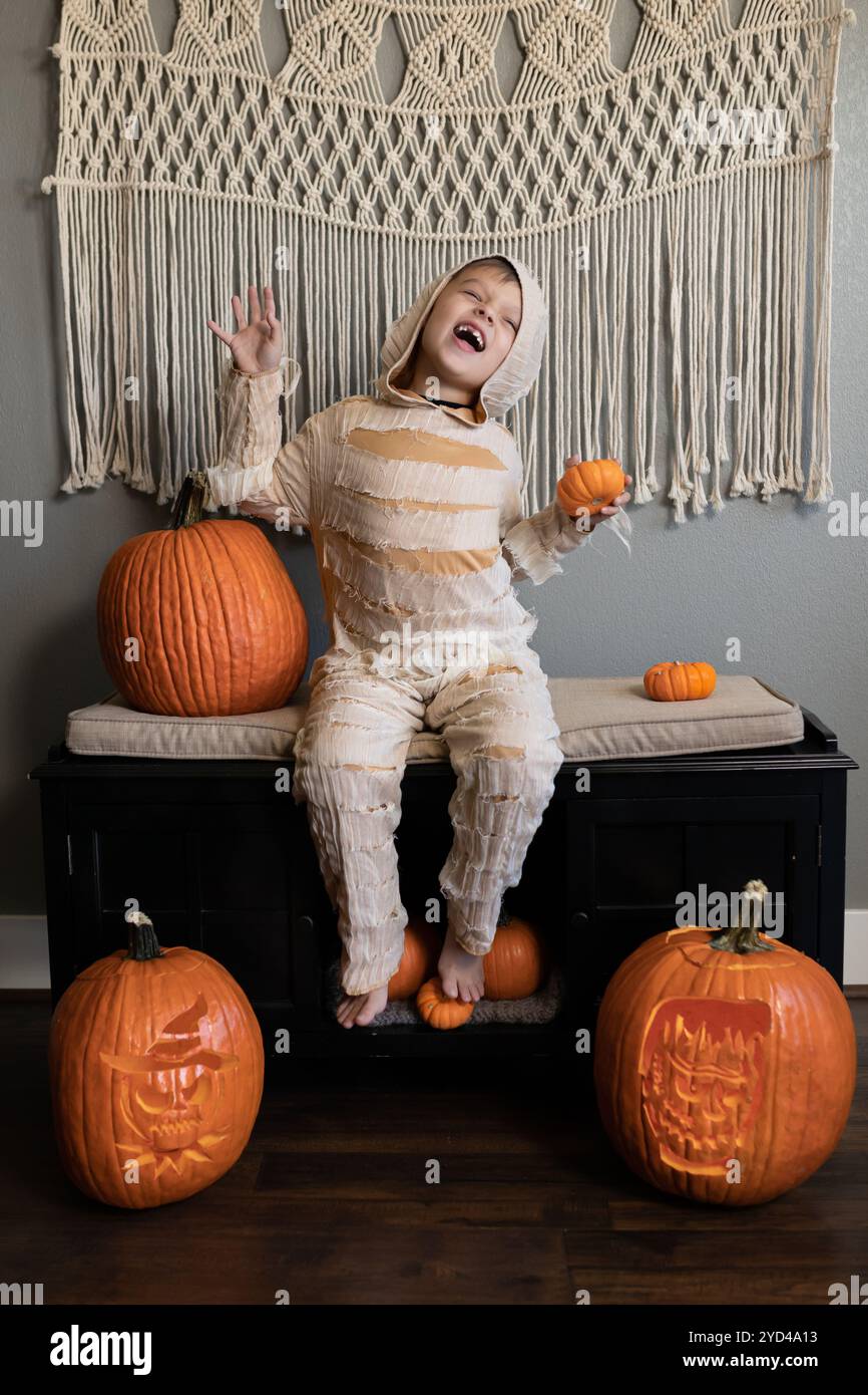 Kind im Mumienkostüm posiert mit Kürbissen in der Halloween-Szene drinnen Stockfoto