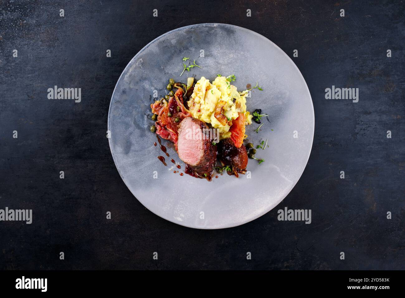 Traditionelles gebratenes Wildhasenfilet mit Pflaumen, Kapern und Kartoffelsalat in Rotwein-Jus serviert als Blick von oben auf dem nordischen Design-Teller mit Kopierraum Stockfoto