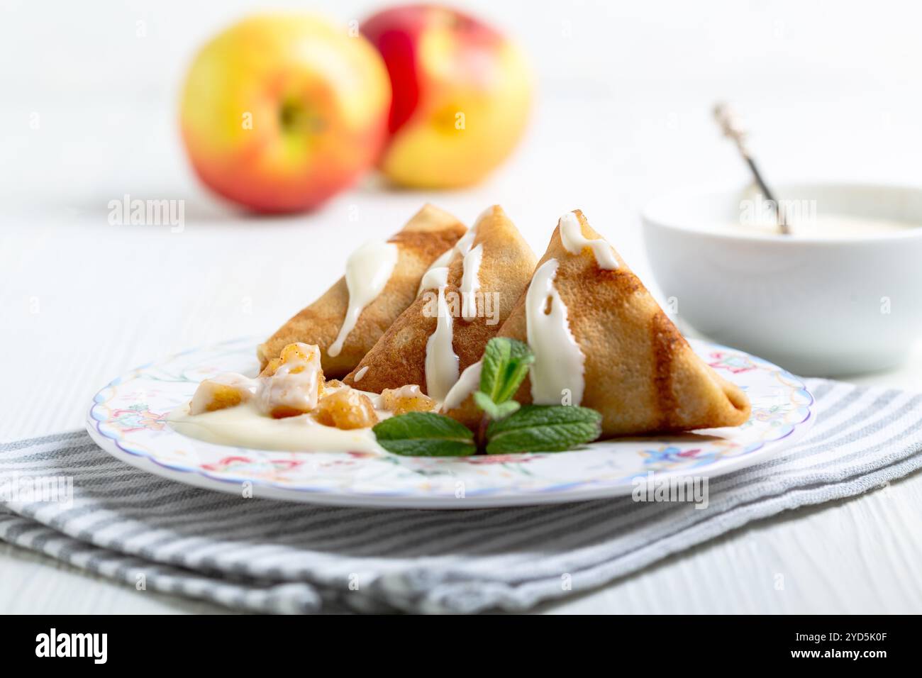 Dreieckige Crepes gefüllt mit Äpfeln mit Zimt, serviert mit Vanillesauce und einem Minzzweig, selektiver Fokus. Stockfoto