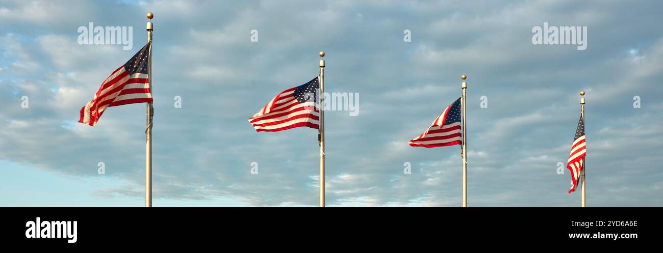 Eine Reihe von vier amerikanischen Flaggen steht hoch und winkt anmutig in der evenziellen Brise vor dem Hintergrund eines teilweise bewölkten Himmels. Stockfoto