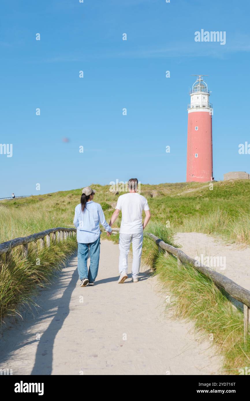 Zwei Personen, die einen malerischen Pfad in der Nähe eines majestätischen Leuchtturms in Texel, Niederlande, entlang schlendern, umgeben von den beruhigenden Geräuschen des Ozeans in den s Stockfoto