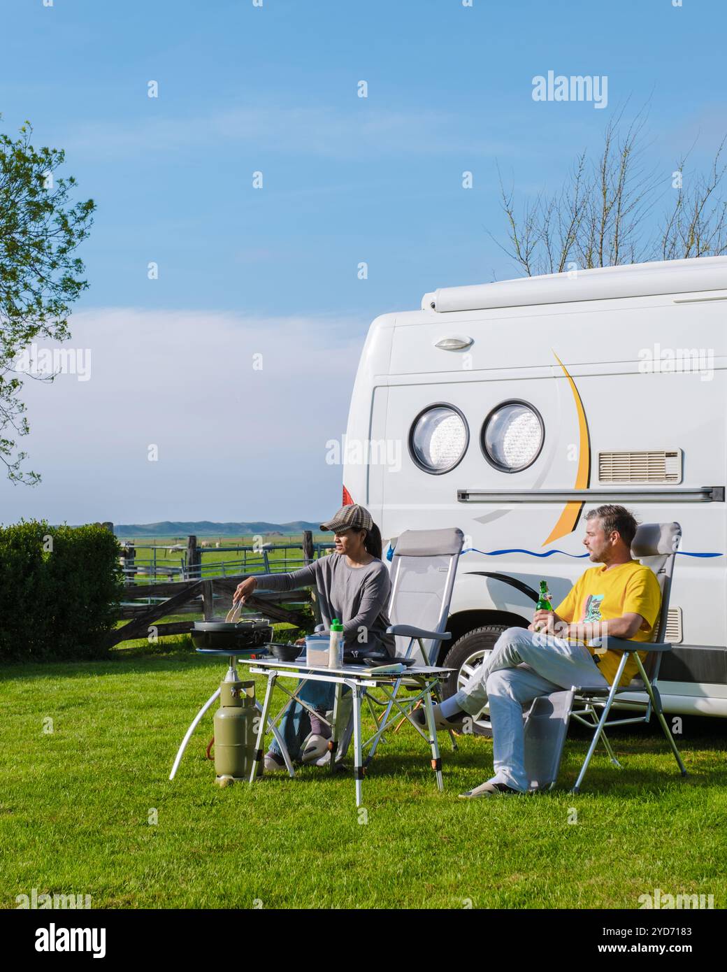 Zwei Personen sitzen vor ihrem Wohnmobil und genießen die friedliche Umgebung eines grasbewachsenen Feldes in Texel, Niederlande Stockfoto