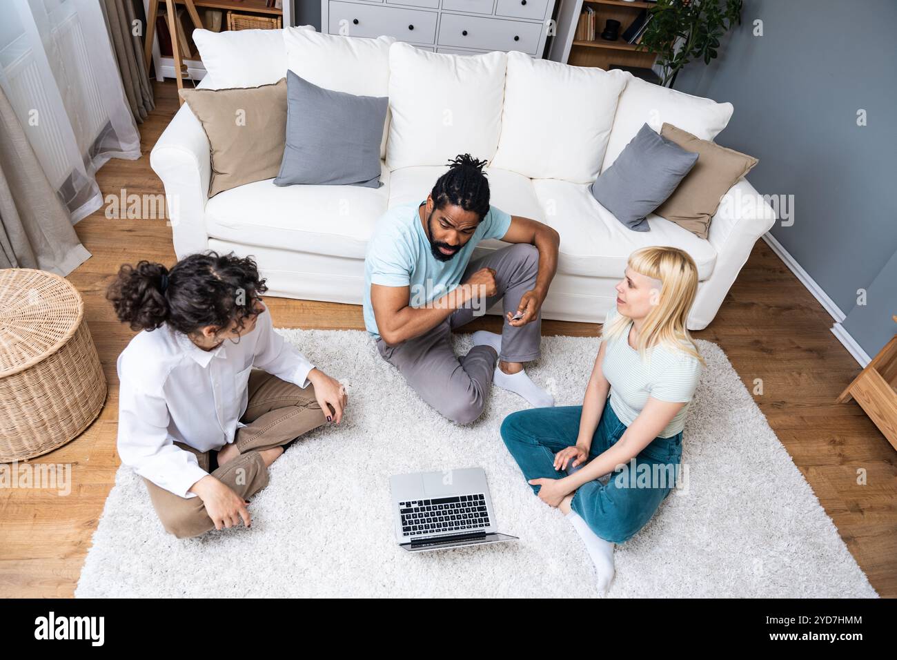 Drei begeisterte Freunde kaufen online eine Reise mit einer Kreditkarte und einem Laptop, die zu Hause auf einem Stockwerk im Wohnzimmer sitzen. pe-Gruppe Stockfoto