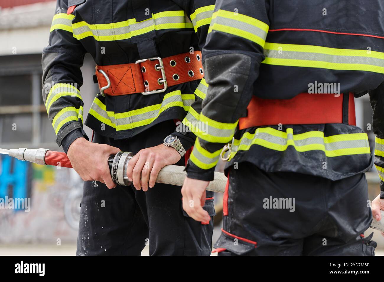 In einer dynamischen Darstellung synchronisierter Teamarbeit arbeiten die Feuerwehrmänner mit Präzision an, um Feuerwehrschläuche zu tragen, zu verbinden und einzusetzen und dabei ihr i zu präsentieren Stockfoto