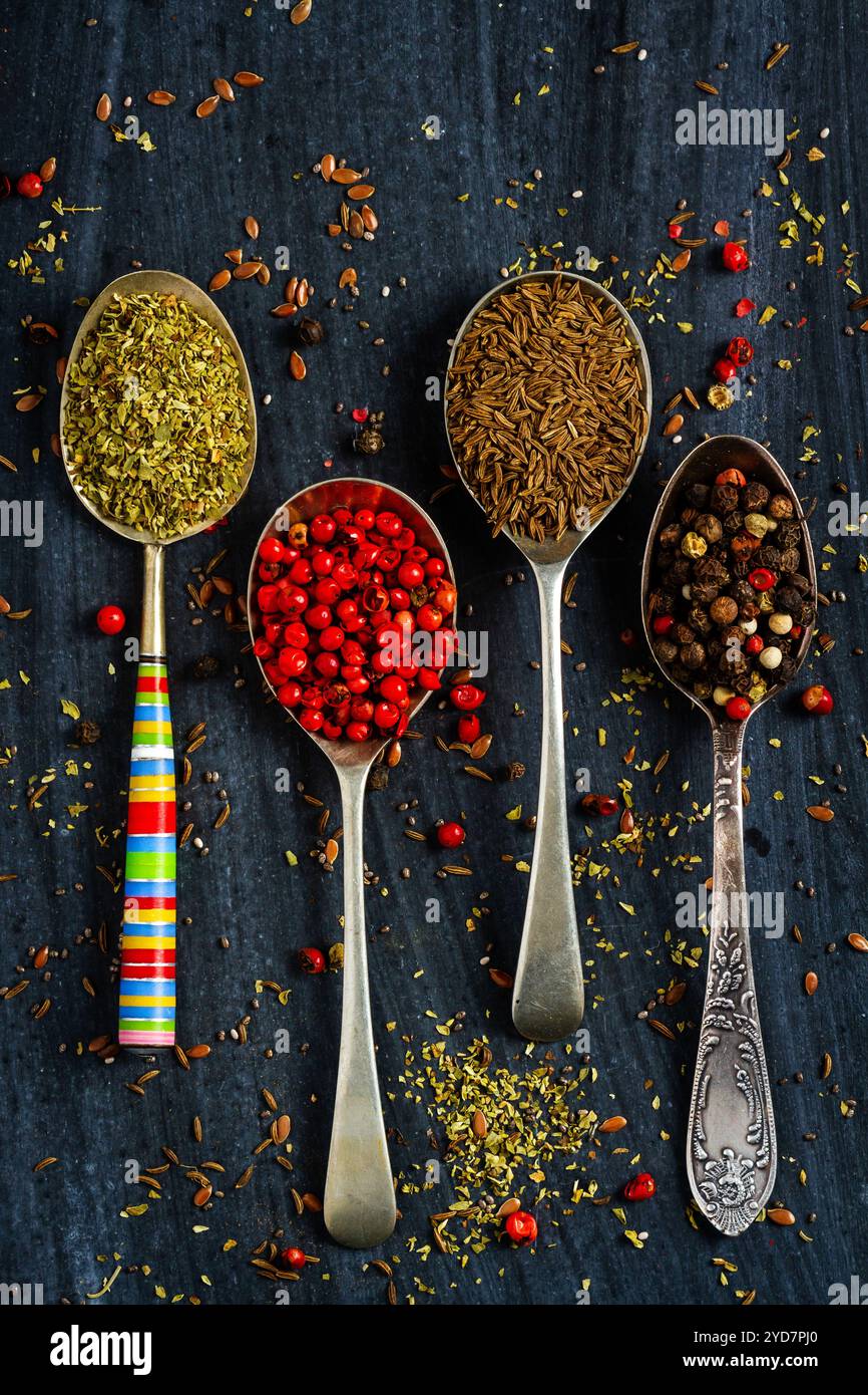 Alte Löffel mit verschiedenen Samen und Gewürzen auf schwarzem Hintergrund. Flach verlegt. Draufsicht. Speisekonzept. Dunkle Stimmungsfotografie. Stockfoto