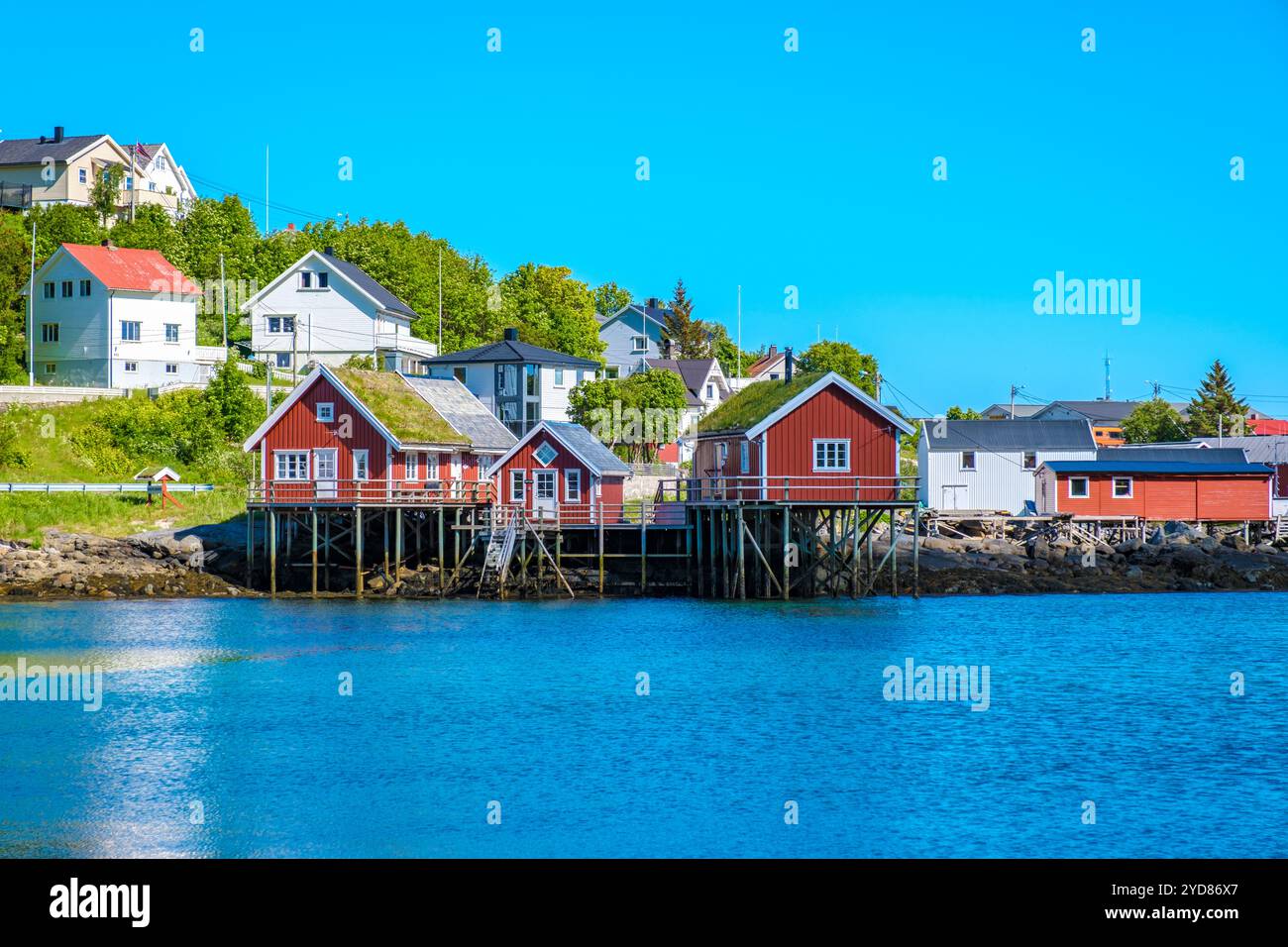 Charmantes Küstendorf in Norwegen mit traditionellen roten Holzhütten auf Stelzen bieten einzigartige Ausblicke auf das ruhige Wasser und die Landschaft. Reine, Lofoten, Norw Stockfoto