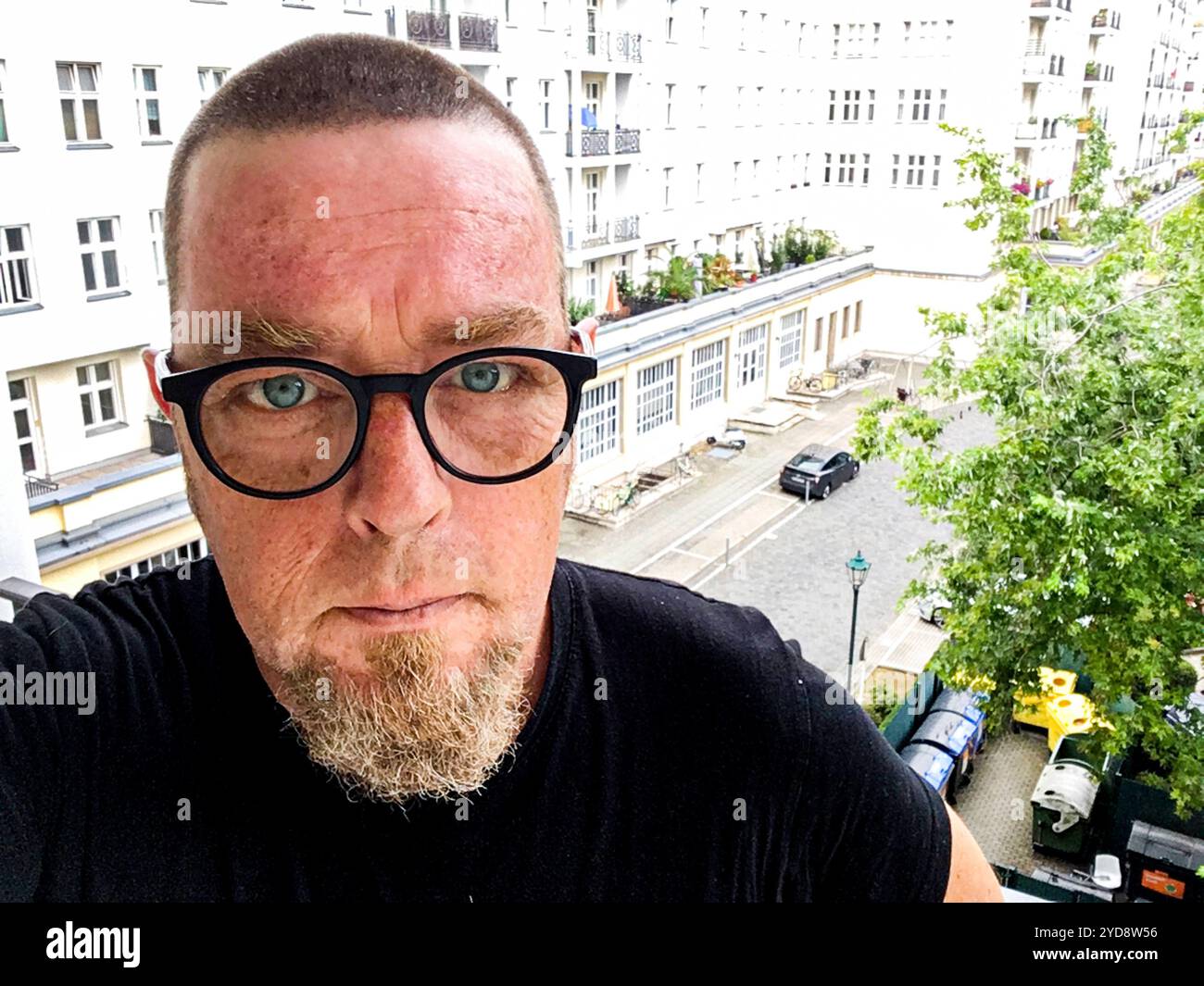 Selfie Mann Selbstporträt Selfie eines beglassenen Mannes mit sehr kurzen Haaren, der auf einem Balkon im dritten Stock mit Blick auf ein Appartementgebäude der Karl Marx Allee steht. Berlin, Deutschland. MR-YES Berlin Koppenstraße Berlin Deutschland Copyright: XGuidoxKoppesxPhotox Stockfoto