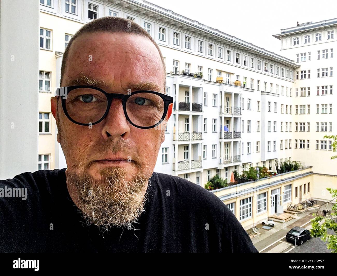 Selfie Mann Selbstporträt Selfie eines beglassenen Mannes mit sehr kurzen Haaren, der auf einem Balkon im dritten Stock mit Blick auf ein Appartementgebäude der Karl Marx Allee steht. Berlin, Deutschland. MRYES Berlin Koppenstrasse Berlin Deutschland Copyright: XGuidoxKoppesxPhotox Stockfoto