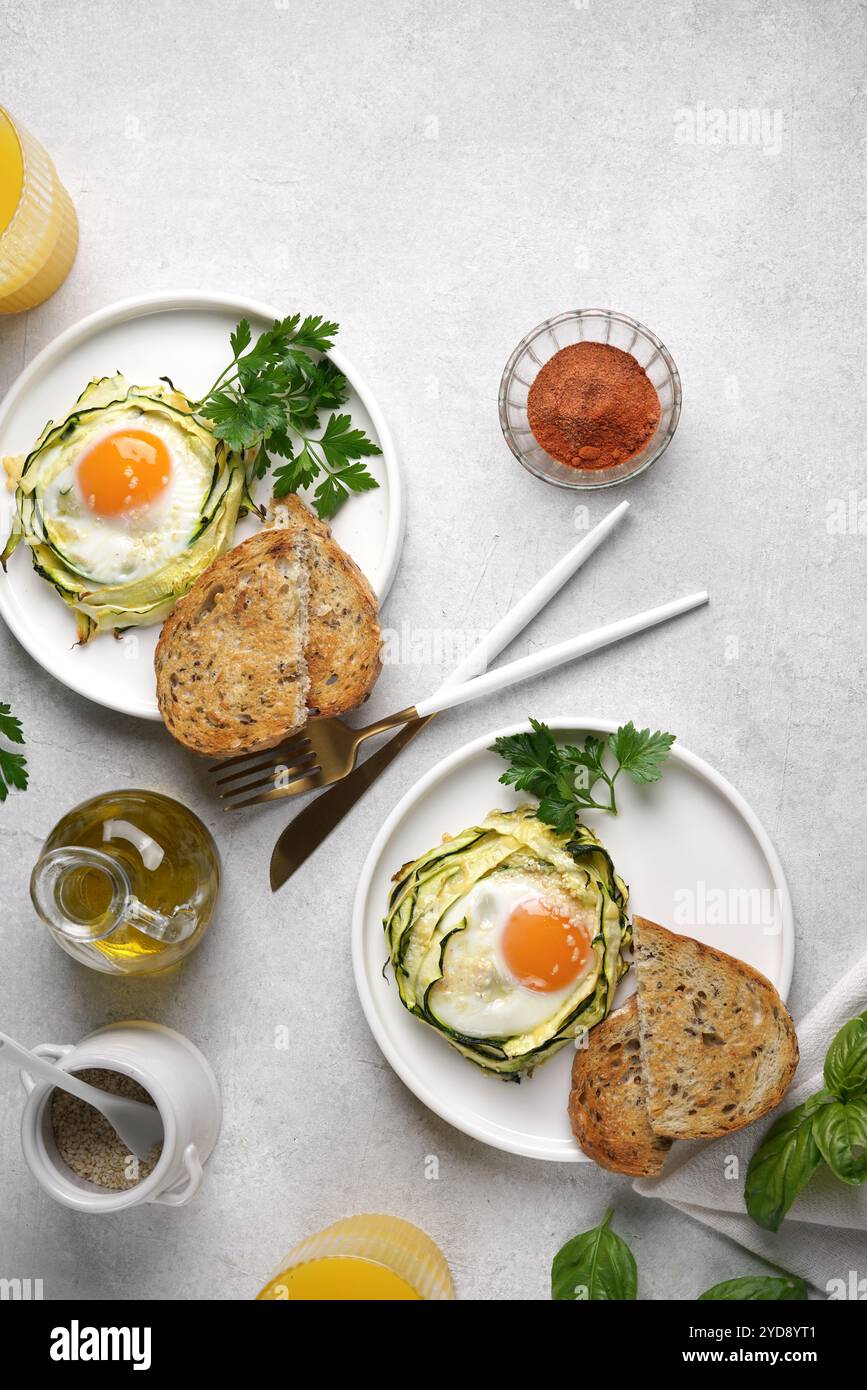 Zwei Teller mit Spiegeleiern in Zucchini-Nudelnestern mit Sesam und Saft im Glas, gesundes Frühstück, vertikaler Blick von oben, Kopierraum Stockfoto