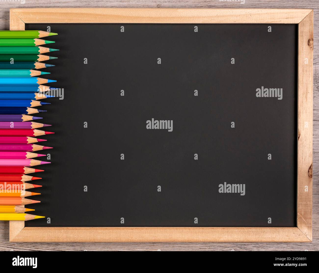 Scharfe Buntstifte sind ordentlich auf einer schwarzen Tafel mit Kopierraum angeordnet. Close-up: Schule - Schreibwaren. Stockfoto